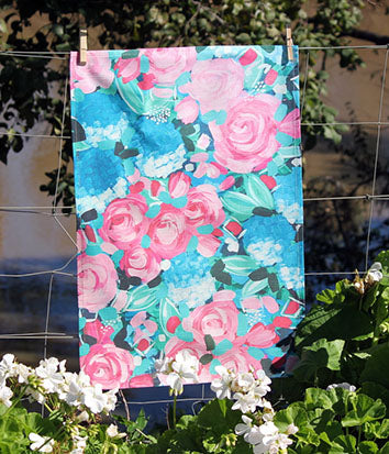 bec fing floral tea towel in pinks and blues hanging on clothesline with in garden